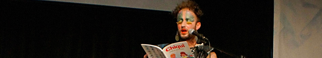 Hombre maquillado leyendo una cartilla titulada "Chiqui"