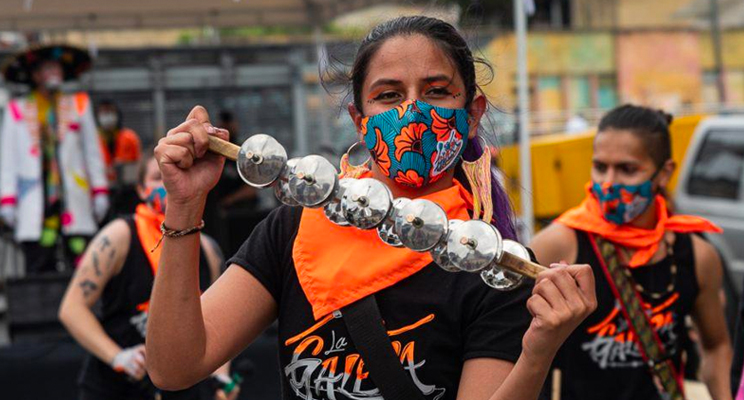 Mujer interpretando instrumento de metales en la calle acompañada de la comparsa que la sigue