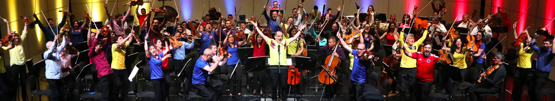 Fotografía de la orquesta completa levantando la mano y con rostros de felicidad
