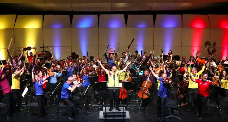 Fotografía de la orquesta completa levantando la mano y con rostros de felicidad