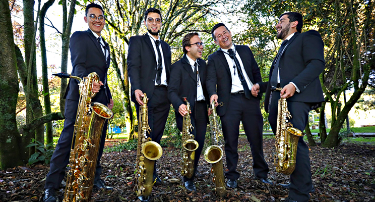 Fotografía de los cinco saxofonistas de cámara en un parque sonriendo