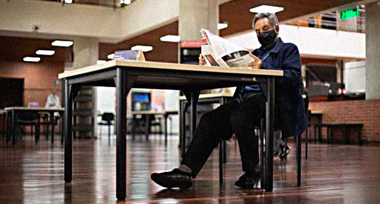 Fotografía de un adulto mayor leyendo un periódico en la biblioteca