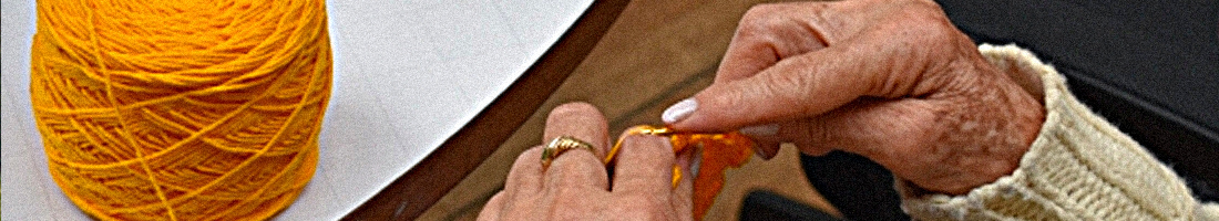Fotografía de las manos de una señora adulta mayor tejiendo con lana de color amarillo quemado