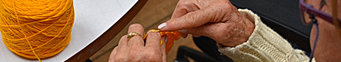 Fotografía de una señora de la tercera edad tejiendo con lana de color amarillo
