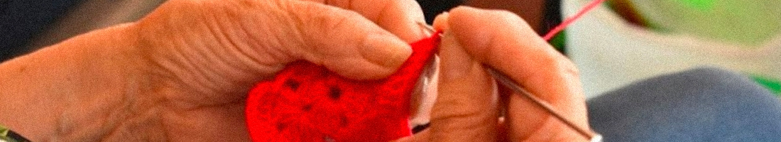 Fotografía de unas manos de una señora tejiendo en lana roja.