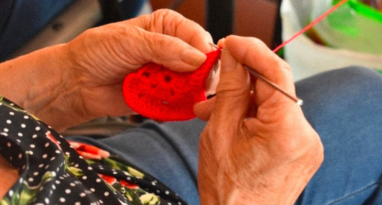 Fotografía de unas manos de una señora tejiendo en lana roja.