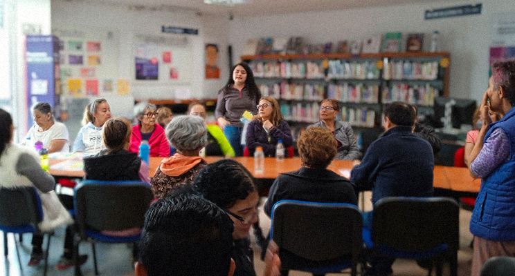 Grupo de adultas mayores en la biblioteca debatiendo.