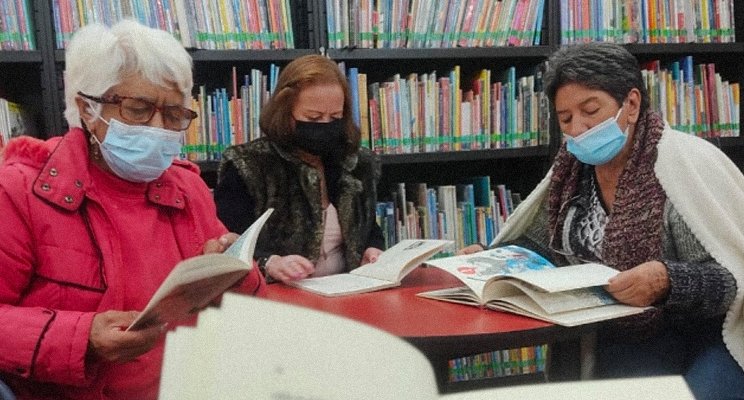 Tres adultas mayores leyendo en la biblioteca.