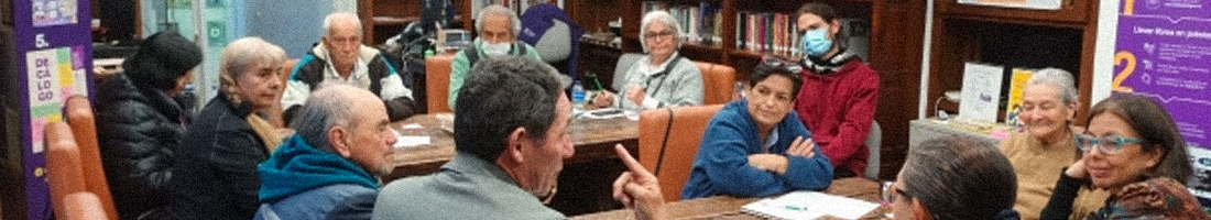 Personas mayores debatiendo en espacio de taller en la biblioteca.