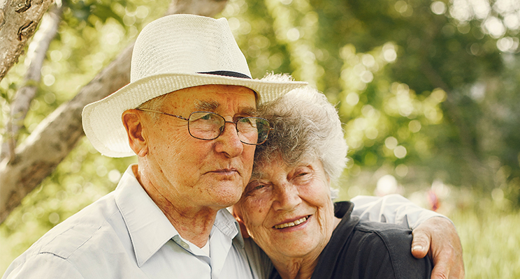Dos adultos mayores (Mujer y Hombre) abrazados con expresión de tranquilidad y felices.