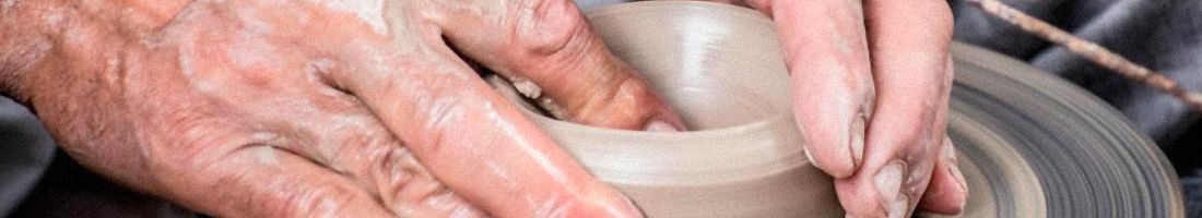 Manos de un adulto mayor sobre un torno modelando una figura de cerámica