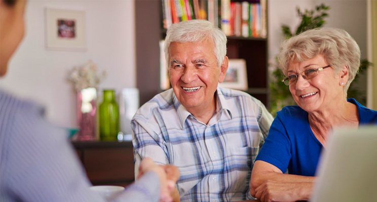 Dos adultos mayores (Mujer y Hombre) sonriendo frente a un asesor que los guia