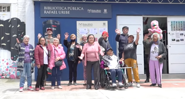 Grupo de personas adultas mayores sonriendo y saludando en la entrada de la Biblioteca Pública Rafael Uribe Uribe