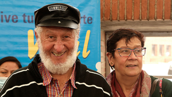 Fotografía de dos adultos mayores, un hombre con barba blanca sonriendo y una mujer con gafas mirando hacia su izquierda