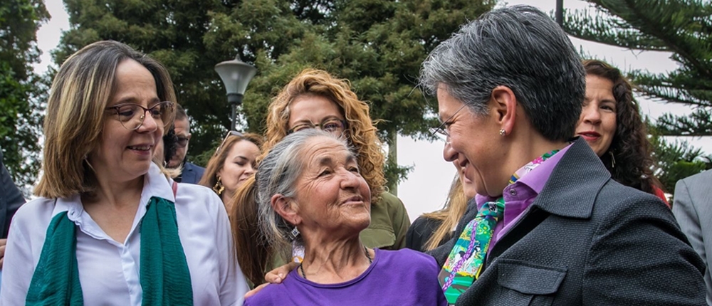 Foto donde aparece la Alcaldesa Claudia López acompañada de una señora de la tercera edad sonriendo y a su lado otra directiva distrital.